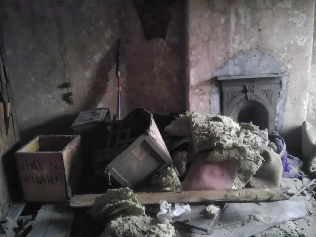 Neglected residential room before refurbishment, with debris and an original fireplace